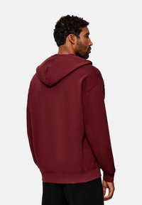 Sudadera burdeos hecha de un tejido suave, con capucha ajustable, corte holgado y puños y dobladillo acanalados. Sin patrones ni gráficos visibles.