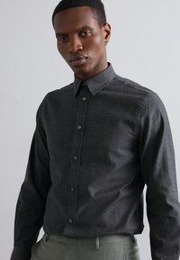 Dark gray button-up shirt made of textured fabric, featuring a classic collar, front placket with buttons, and long sleeves.