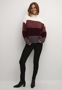 Maglione pesante a maglia con un design a blocchi di colore in bianco, malva, bordeaux e grigio. Maniche lunghe con texture a coste. Abbinato a jeans skinny neri.