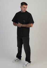 Camiseta negra de manga corta con un logo blanco, combinada con pantalones oscuros y zapatillas blancas con detalles grises. Textura suave de algodón.