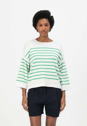Weißer Pullover mit grünen horizontalen Streifen, überschnittenen Schultern und rundem Ausschnitt, kombiniert mit marineblauen Shorts. Glatte Stofftextur.