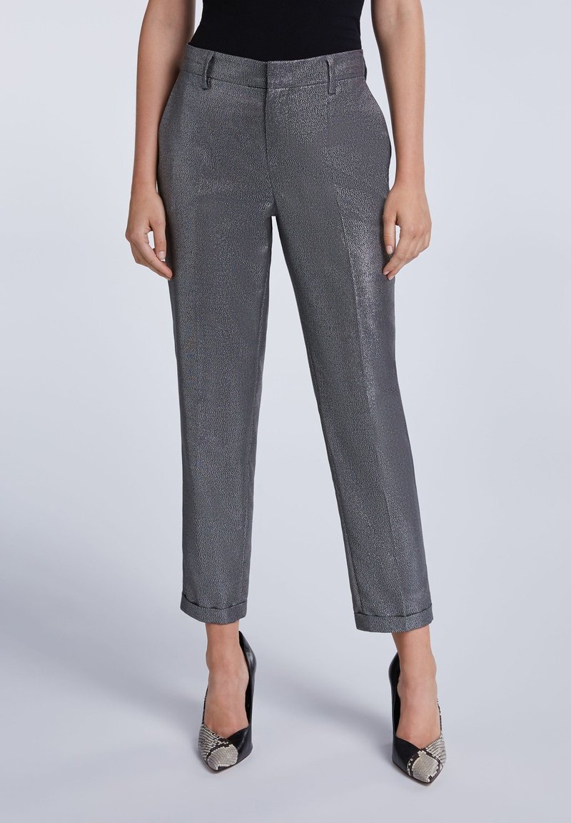Femme portant un pantalon tailleur gris métallisé aux chevilles et des talons hauts noirs à bout pointu avec un motif peau de serpent sur les orteils.