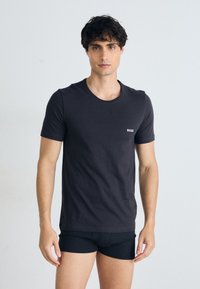 Schwarzes Baumwoll-T-Shirt mit kurzen Ärmeln, Rundhalsausschnitt und kleinem weißen "BOSS"-Logo auf der linken Brust. Verfügt über ein tailliertes Design.