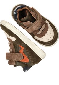 Bruine en beige sneakers van suède en leer. Kenmerken zijn onder andere klittenband, geperforeerde neus en oranje accenten.