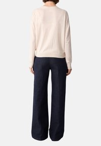 Maglione lungo con maniche, di colore beige chiaro e realizzato in materiale morbido, abbinato a pantaloni in denim scuro a vita alta e gamba larga. Design semplice, senza motivi visibili.