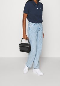 Marinblå polo skjorta med tre-knapp stängning, ljusblå raka jeans, vita sneakers och en liten svart handväska med handtag.