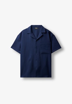 Chemise bleu marine à manches courtes avec boutons, col camp et une poche poitrine, posée à plat sur fond blanc.