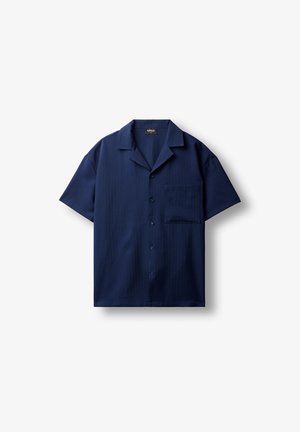 Chemise bleu marine à manches courtes avec boutons, col camp et une poche poitrine, posée à plat sur fond blanc.