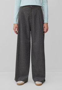 Pantalons larges gris avec plis, fabriqués à partir d'un tissu texturé. Fermeture à bouton à la taille, associés à des baskets blanches avec des semelles beiges.