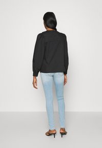 Chaqueta negra de mangas abullonadas con yugo trasero, combinada con jeans ajustados de color azul claro, llevada con sandalias de tacón negras.