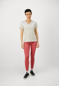 Világosszürke, rövid ujjú, V nyakú póló, amelyet rózsaszín leggings-szel párosítanak. A modellen fekete sportcipők találhatók, fehér részletekkel. Egyszerű, testhezálló dizájn.