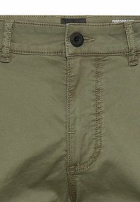Close-up of olive green pants waistband with black button, belt loops, and visible stitching details.