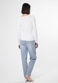 Camisa blanca de manga larga combinada con jeans ajustados de lavado claro. La camisa presenta un cuello redondo y puños acanalados, mientras que los jeans tienen un dobladillo deshilachado.
