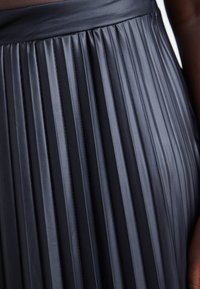 Gonna nera plissettata realizzata in materiale lucido, con pieghe verticali nette e una fascia in vita liscia, che mette in risalto una texture elegante.
