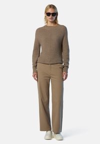 Brauner Strickpullover mit Rundhalsausschnitt und gerippten Bündchen, kombiniert mit beigen weiten Hosen und weißen Sneakers. Schwarze Sonnenbrille rundet den Look ab.