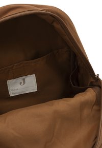 Interieur van een bruine stoffen rugzak met een ritsopening, voorzien van een labelvak en een zachte, gestructureerde voering. Minimalistisch ontwerp.
