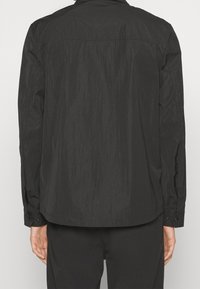 Black lightweight jacket with a textured surface, long sleeves, and buttoned cuffs. Features a point collar and a straight hemline.