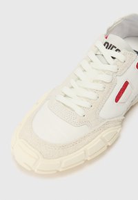 Basket avec une tige en maille blanche, des accents en daim gris texturé, des lacets blancs et des détails rouges, dotée d'une épaisse semelle en caoutchouc crème.