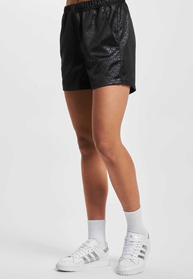 Shorts noirs avec un motif texturé, taille élastique et coupe décontractée, associés à des baskets blanches et des chaussettes.