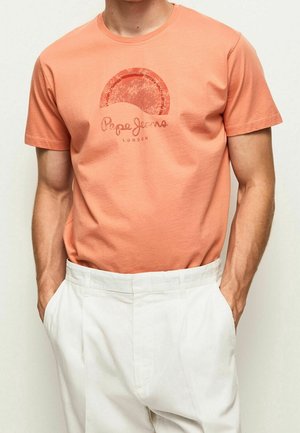 Korallefarbene Baumwoll-T-Shirt mit einem verblassten roten Grafikdesign eines Halbkreises und dem Text "Pepe Jeans London" darunter. Rundhalsausschnitt, kurze Ärmel.