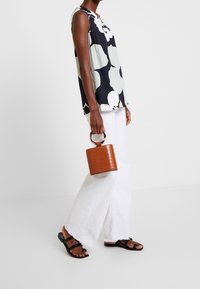 Top floreale senza maniche bianco e nero, jeans bianchi a gamba larga, sandali neri, con una borsa marrone testurizzata con manico circolare.