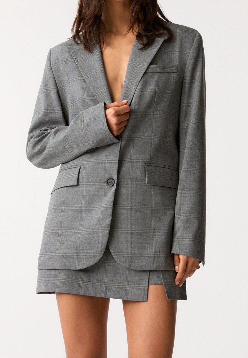 Grå rutig blazer med notchade slag, enknapsstängning och två framfickor, ihop med en matchande kort kjol.