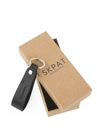 Llavero de cuero negro con acabado texturizado, unido a un anillo metálico redondo, colocado sobre una caja de cartón marrón con el nombre de la marca visible.