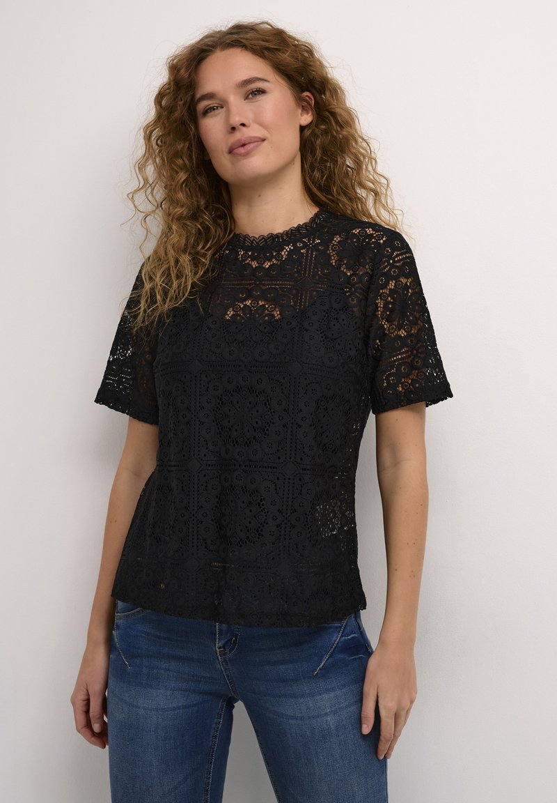 Black lace top featuring a geometric pattern, short sleeves, and a scalloped neckline. Paired with blue jeans, highlighting a relaxed fit.