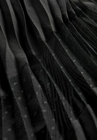 Tissu noir plissé avec un bas en maille texturée. La maille présente de subtils pois, créant un contraste avec les plis lisses au-dessus.