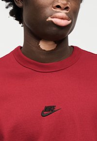 Κόκκινο βαμβακερό φούτερ με στρογγυλή λαιμόκοψη και μικρό μαύρο λογότυπο Nike στην αριστερή πλευρά του στήθους. Ομαλή υφή, λιτός σχεδιασμός.