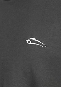 Dunkelgrauer Stoff mit strukturiertem Finish und einem gestickten weißen Logo auf der Brust, das ein schlankes Design zeigt.