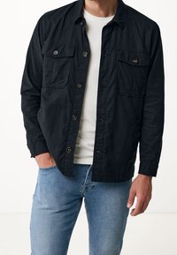 Black button-up shirt with two chest pockets, featuring a relaxed fit and long sleeves, paired with light blue jeans.