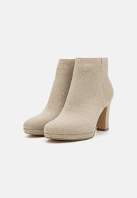 Beżowe botki za kostkę o teksturowanym, metalicznym wykończeniu i zwężonych wysokich obcasach. Okrągły czubek i gładka, czysta sylwetka.