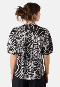 Black and white blouse with a flowing zebra pattern, featuring puff sleeves, a gathered back, and a soft, lightweight fabric.
