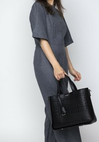 Zwarte leren tote bag met ingewikkelde uitsnijdingen, gestructureerd ontwerp, dubbele handvatten aan de bovenkant en metalen hardware accenten.