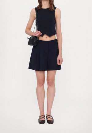 Námořnicky modrý crop top s vlnitým lemem, doplněný rozšířenou námořnicky modrou sukní. Černá texturovaná kabelka přes rameno a hnědé baleríny se pásky doplňují vzhled.