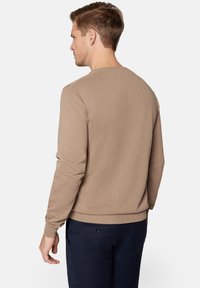 Beżowy sweter dziany z długimi rękawami, okrągłym dekoltem i ściągaczami. Gładka struktura z subtelnym detalem szycia z tyłu.