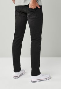 Mustad slim-fit teksad, millel on sile tekstuur, viie-tasku disain ja õrn pleekimine; koos valgete madala varbaga tossudega, millel on punased aktsendid.