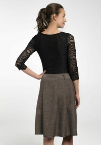 Schwarze Spitzenbluse mit Dreiviertelärmeln, kombiniert mit einem braunen, knielangen Rock, der einen strukturierten Bund und ein plissiertes Design aufweist.