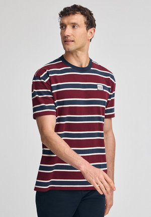 Mørkerød og marineblå stribet t-shirt med rund hals og korte ærmer. Har et lille hvidt logo-patch på brystet. Lavet af bomuldsstof.