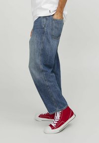 Jeans de mezclilla azul con un diseño de pierna recta, cintura de altura media, lavado desgastado y bolsillos laterales, combinados con zapatillas rojas de caña alta.