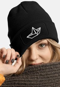 Black ribbed beanie with a fitted design, featuring a white origami boat graphic on the front. Material texture appears soft and stretchy.