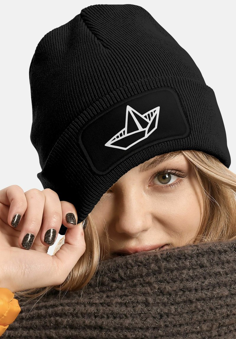 Black ribbed beanie with a fitted design, featuring a white origami boat graphic on the front. Material texture appears soft and stretchy.