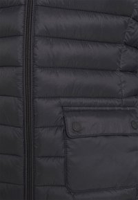 Czarna pikowana kurtka z poziomą teksturą, z przednim zamkiem błyskawicznym i kieszenią na zatrzask po lewej stronie.