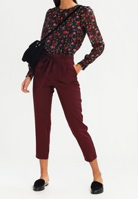 Blusa nera a fiori con maniche lunghe, pantaloni borgogna a vita alta e sandali neri con dettagli in pelliccia. Borsa a tracolla nera lucida.