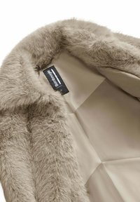 Cappotto in pelliccia sintetica beige con una fodera liscia simile alla seta e un'etichetta nera BomBoogie cucita all'interno dell'area del colletto.