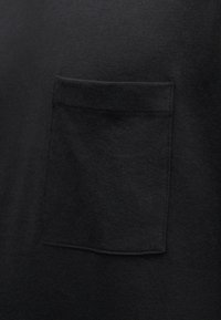 Μαύρο κοντό μανίκι μπλουζάκι από μαλακό βαμβάκι, με μια ραμμένη τσέπη στην αριστερή πλευρά και λεία, ομοιόμορφη υφή.