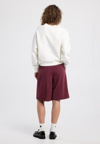 Valkoinen oversized huppari, maroonit shortsit, jämäkkä kangas, rento malli. Mustat kengät ja valkoiset sukat sydänkuviolla. Siisti, minimalistinen design.