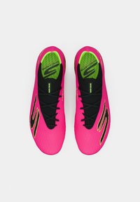 Kirkkaan vaaleanpunaiset urheilu kengät mustilla yksityiskohdilla, joissa on teksturoidut päälliset, mustat nauhat ja vihreä pohjallinen logotarkkuudella.