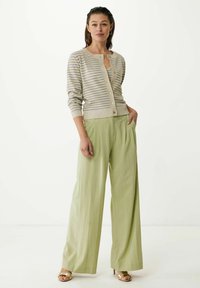 Randig cardigan i beige och lavendel; lätt stickad med knappar. Flödande, högmidjade, ljusgröna byxor med sidofickor. Guld sandaler.